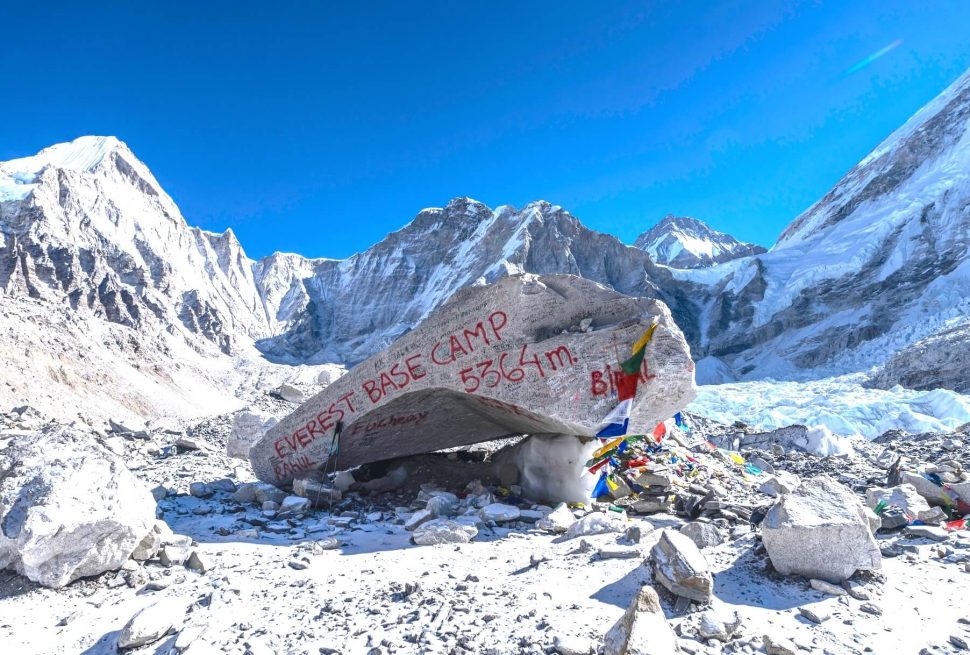 A lone trekker standing on a snow-covered trail with Mount Everest in the clear blue background during winter.